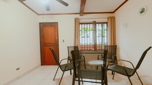 A room with a wooden door, a window with metal bars, a ceiling fan, and a table with chairs. - Quepos Inn (Quepos)