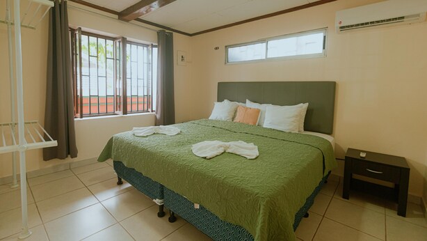 A hotel room with a large bed, a nightstand, a window with curtains, and a ceiling fan. - Quepos Inn (Quepos)