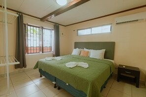 A hotel room with a large bed, a nightstand, a window with curtains, and a ceiling fan. - Quepos Inn (Quepos)