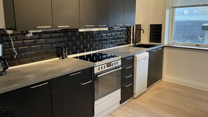 A modern kitchen with black cabinets, a stainless steel countertop, a built-in oven, and a dishwasher.