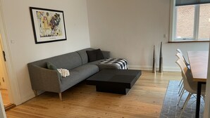 A modern living room with a grey sectional sofa, a black coffee table, and a dining area with a wooden table and chairs.