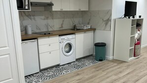 A compact kitchen with white cabinets, a washing machine, a microwave, and a trash bin. - Studio Bel-Air (Saint-Denis)