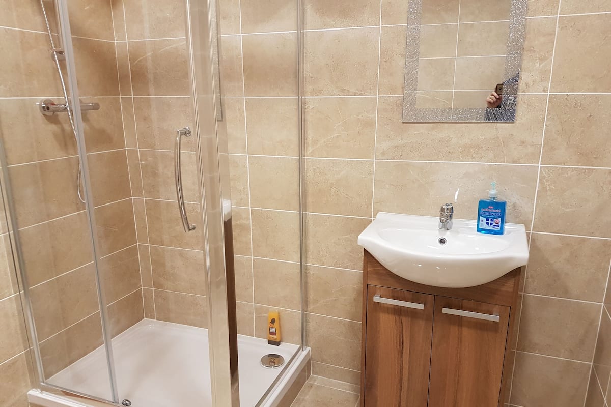 A bathroom with a glass shower enclosure, a white sink with a mirror above it, and a wooden cabinet below.