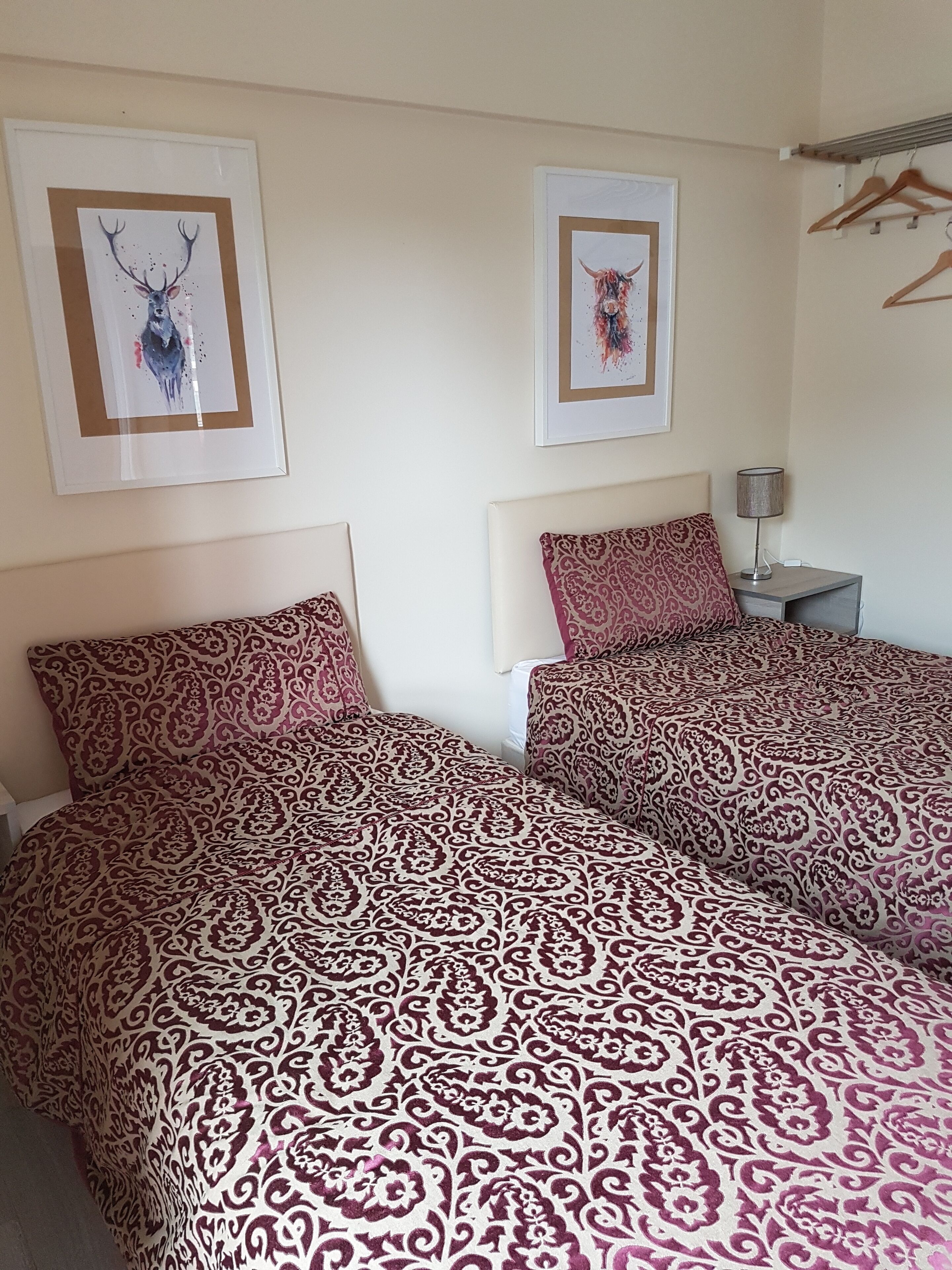 Ein Doppelbett mit gemusterten Bettwäsche, ein Nachttisch mit Lampe und zwei gerahmte Bilder an der Wand.