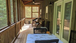 Une véranda couverte avec une table et des chaises, des balustrades en bois et une vue sur l’extérieur.