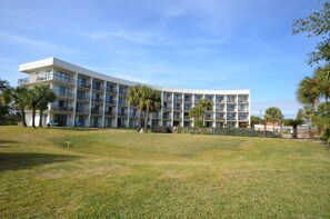 A multi-story hotel with a curved facade, outdoor seating, and palm trees.