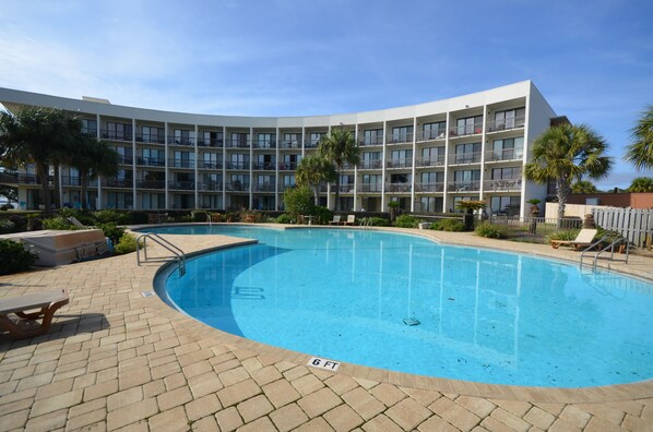A hotel with a swimming pool, multiple balconies, and palm trees.