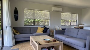 A modern living room with a grey sofa, a wooden coffee table, and a bookshelf. - Ōhope Holiday Home  (Ōhope)