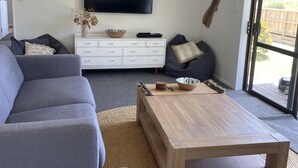 A modern living room with a grey sofa, a wooden coffee table, and a flat-screen TV mounted on the wall. - Ōhope Holiday Home  (Ōhope)
