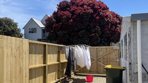 A backyard with a wooden fence, a clothesline with laundry, a red bucket, and a green trash bin. - Ōhope Holiday Home  (Ōhope)