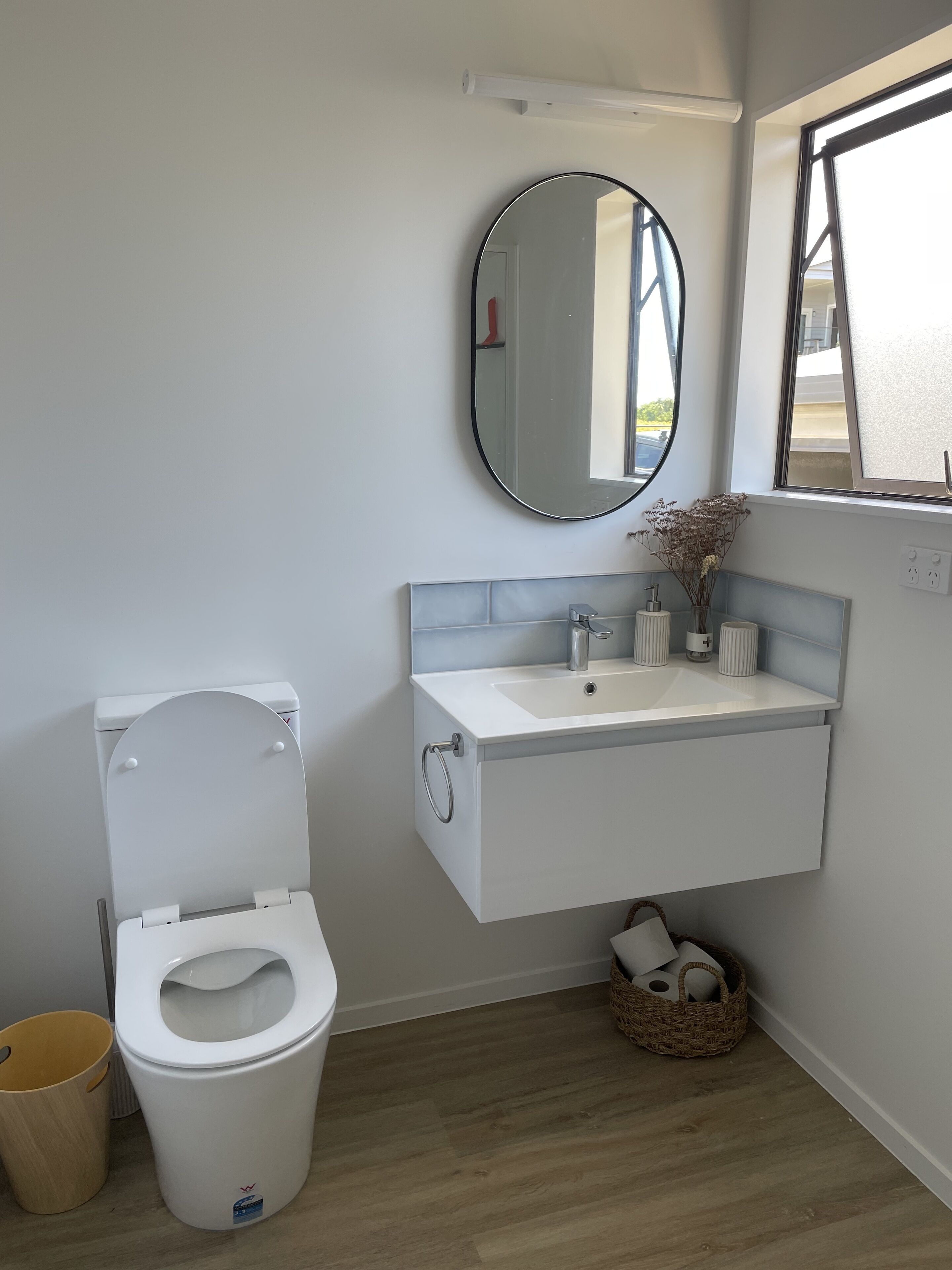 Ein modernes Badezimmer mit Toilette, Waschbecken mit Spiegel und einem Fenster mit Jalousien.
