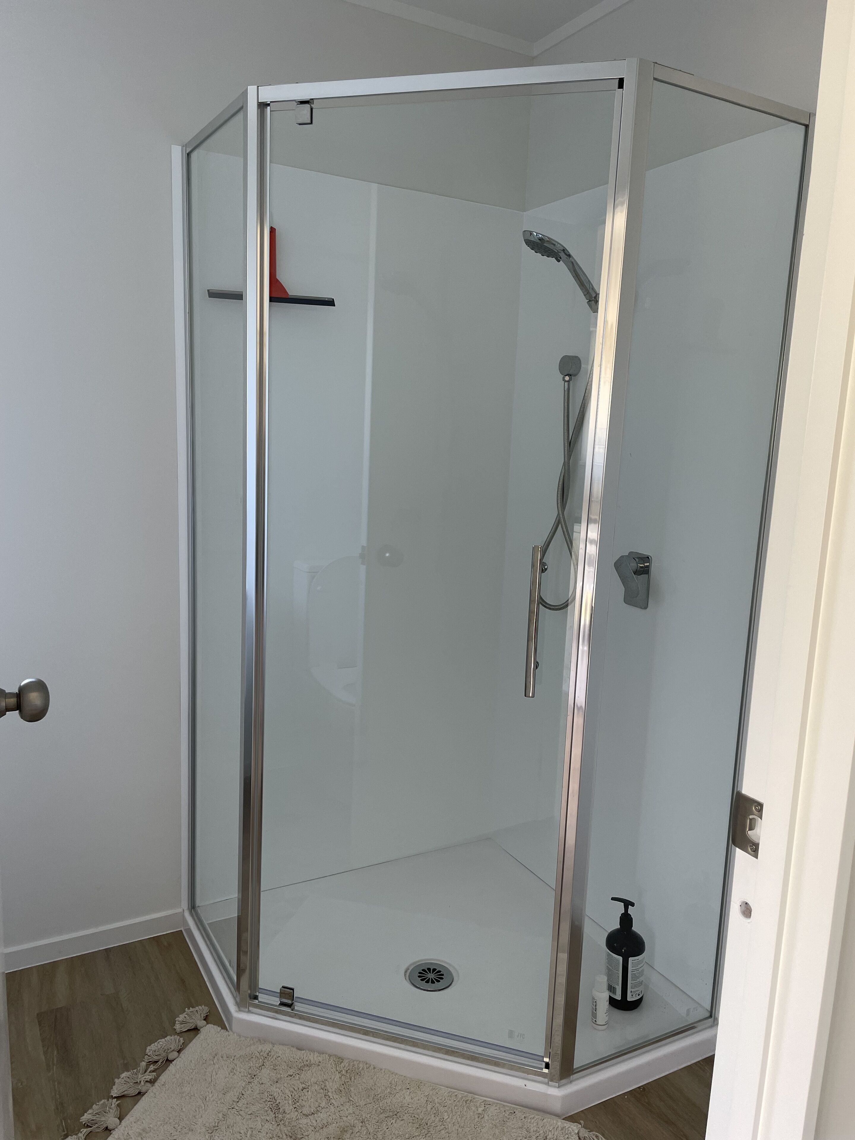 A glass-enclosed shower room with a showerhead, handheld shower, and a bottle of shampoo.