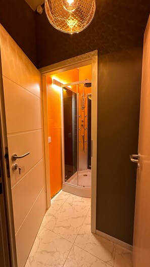 A hallway leading to a bathroom with a glass shower enclosure and a ceiling light fixture. - smart&beautiful Express (Nordkirchen)