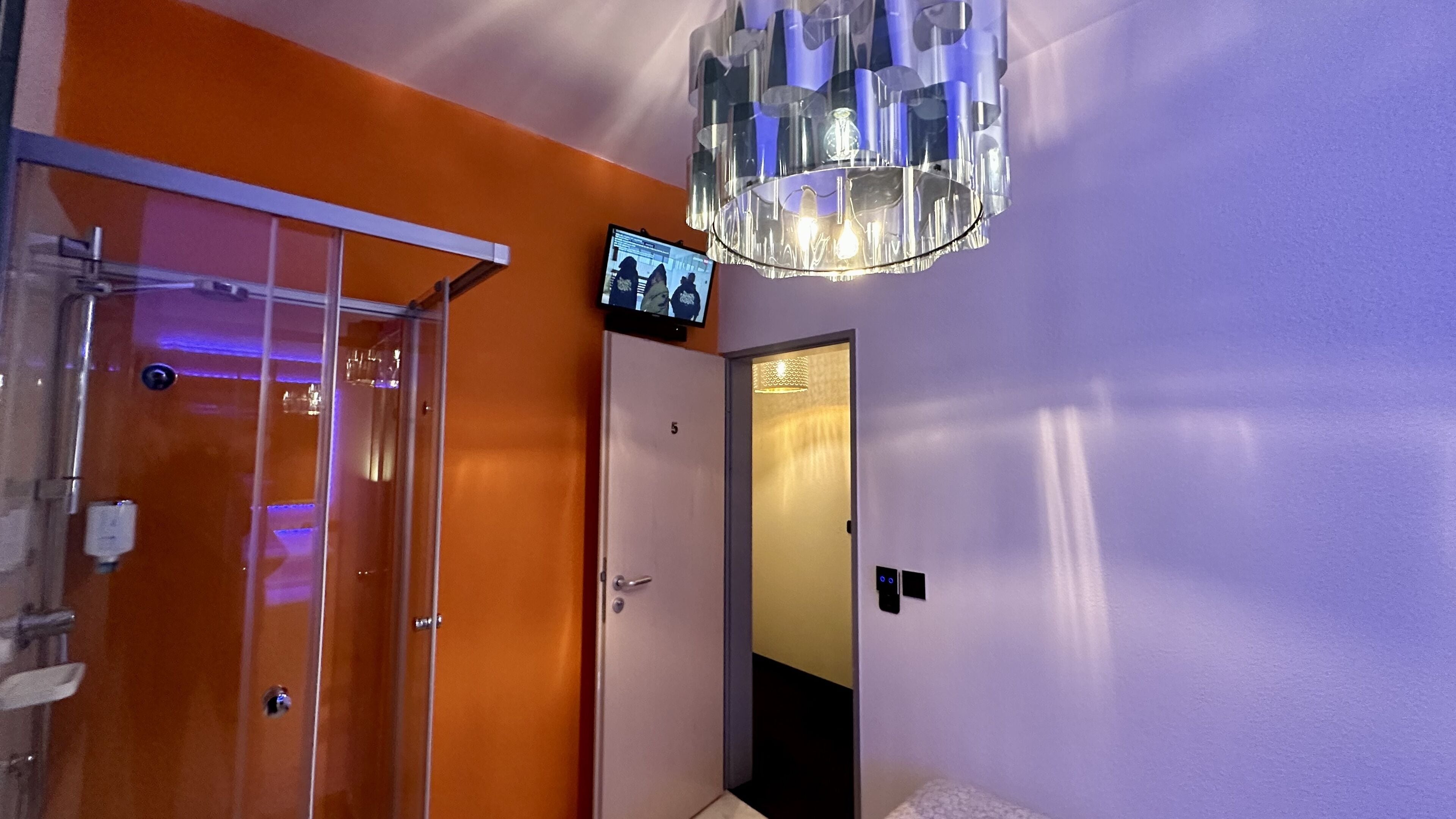 Una habitación con cabina de ducha de vidrio, un televisor montado en la pared y un candelabro.