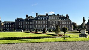 Un edificio grande e histórico con arquitectura simétrica, jardines cuidados y estatuas.