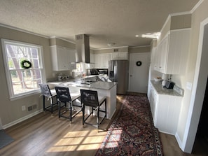 A modern kitchen with white cabinets, a central island with bar stools, a stainless steel refrigerator, and a decorative rug. - Sweet Home Augusta (Augusta)