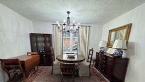 A dining room with a chandelier, wooden table, chairs, a rug, a cabinet, and a mirror.