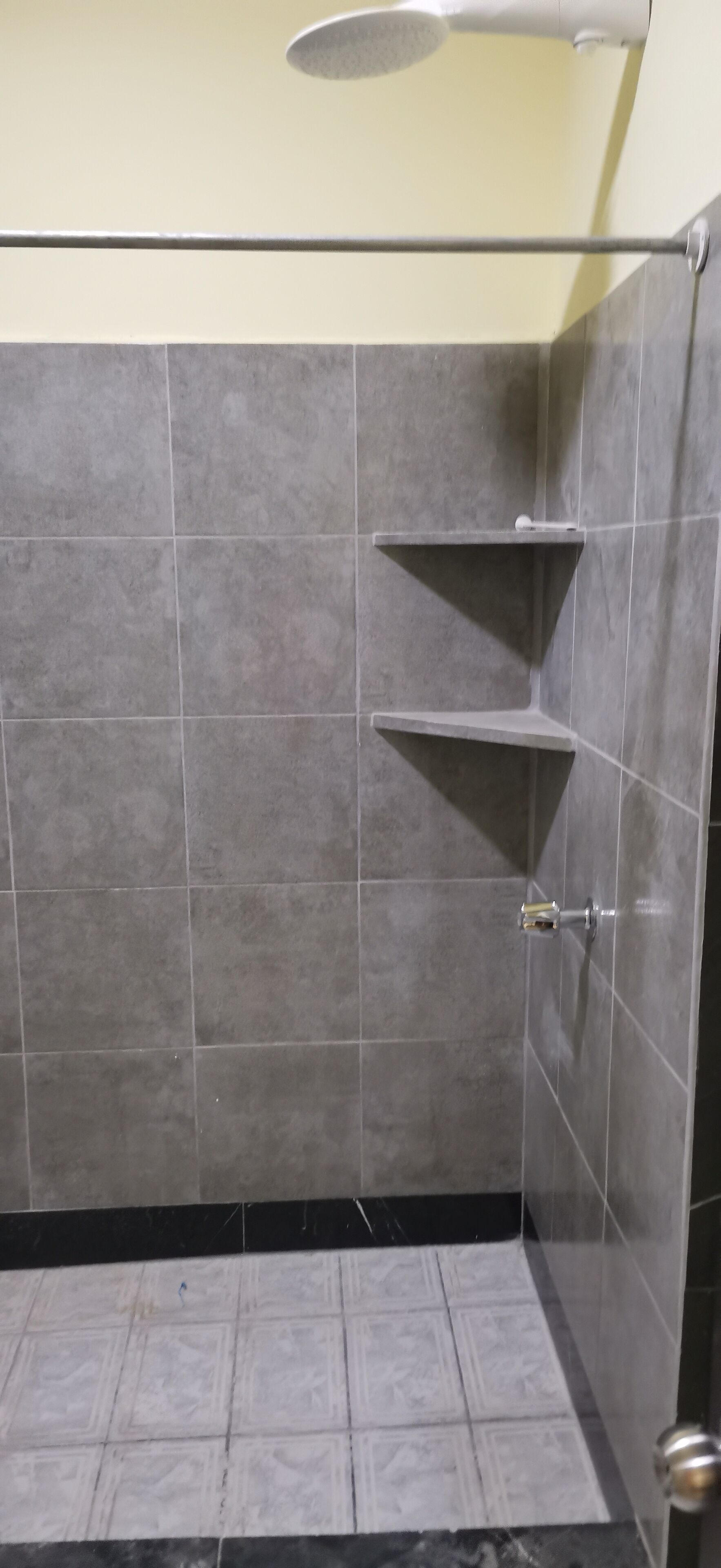 A shower area with grey tiles, a glass shower door, and a metal towel rack.