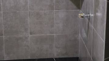 A shower area with grey tiles, a glass shower door, and a metal towel rack.