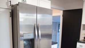 Ein Edelstahl-Kühlschrank mit Wasserspender, weiße Schränke und ein Holzboden in einer Küche.
