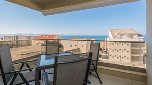 Un balcon avec une table et des chaises, donnant sur une zone côtière avec des bâtiments et la mer.