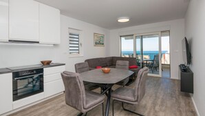 Une cuisine moderne dotée d’un four encastré, d’une table à manger avec quatre chaises et offrant une vue sur la mer grâce à une porte vitrée.