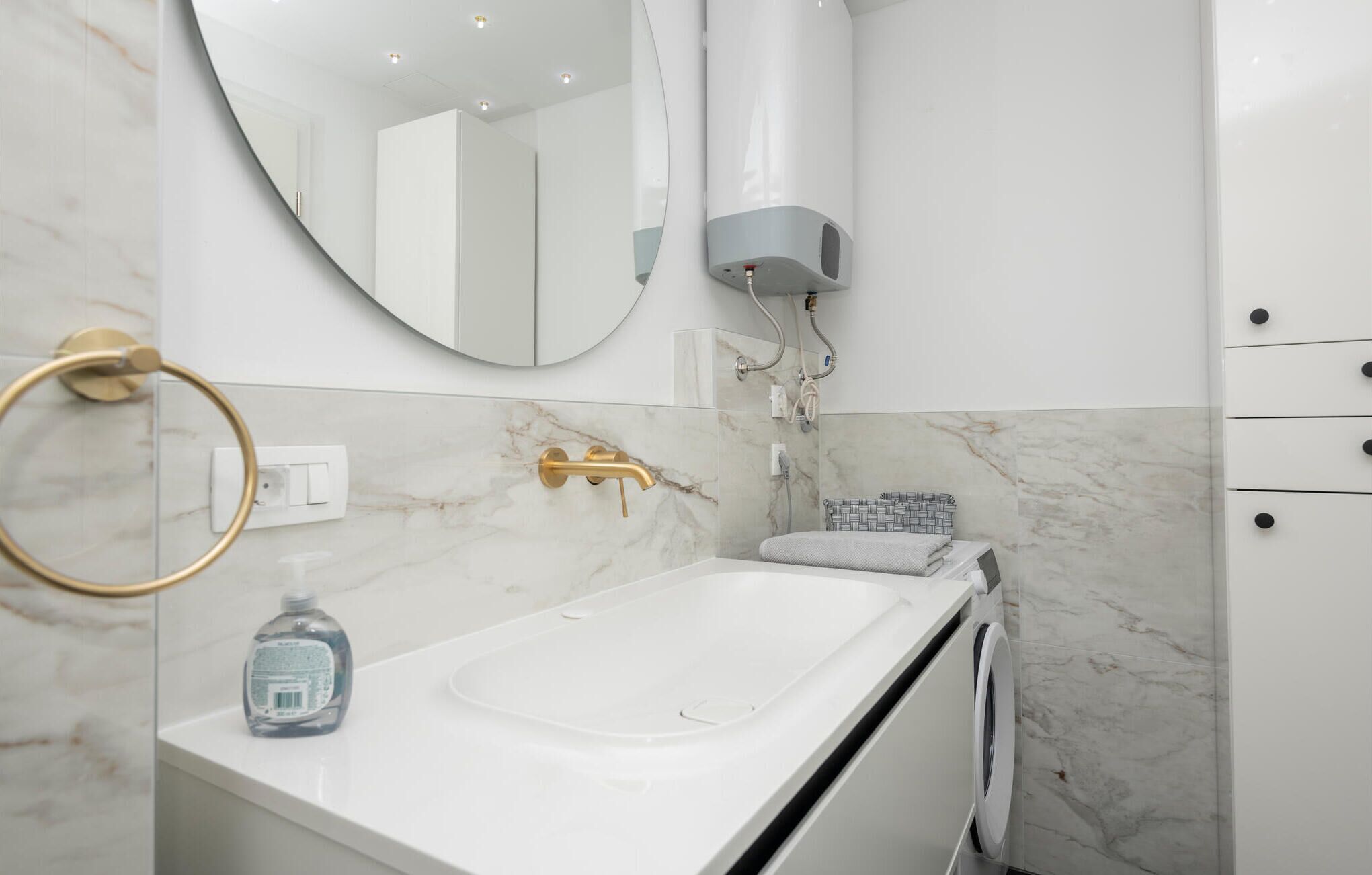 A modern bathroom with a white sink, gold fixtures, a towel rack, and a mirror.