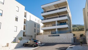 Un immeuble résidentiel à plusieurs étages, doté d’une façade en pierre, avec une voiture garée devant et un ciel dégagé.