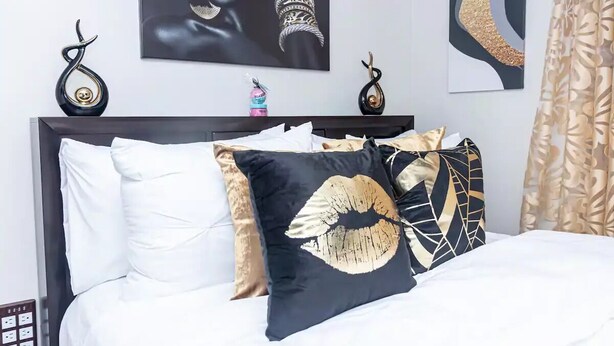 Un letto rifatto con cura, con cuscini bianchi e fantasia, un cuscino decorativo nero e oro, e una parete con arte astratta e due elementi decorativi a forma di serpente.