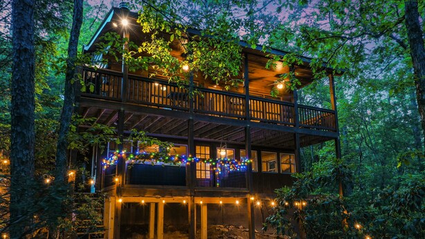 Eine zweigeschossige Holzhütte mit einem Balkon, umgeben von Bäumen.