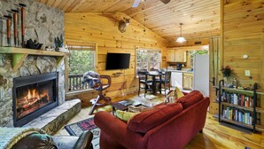Ein gemütliches Blockhaus-Interieur mit Kamin aus Stein, einem roten Sofa, einem Essbereich und einem Bücherregal.