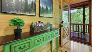 Ein Holzhütten-Innenraum mit einem grünen Schminktisch, einem Korb mit Toilettenartikeln und zwei gerahmten Waldmotiven.