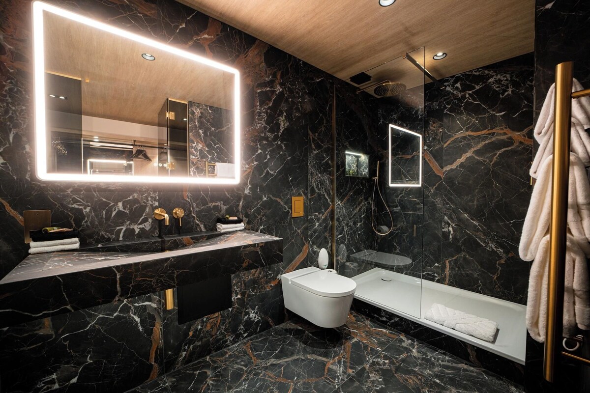 A modern bathroom with a marble floor, a large mirror, a toilet, a bathtub, and a towel rack.
