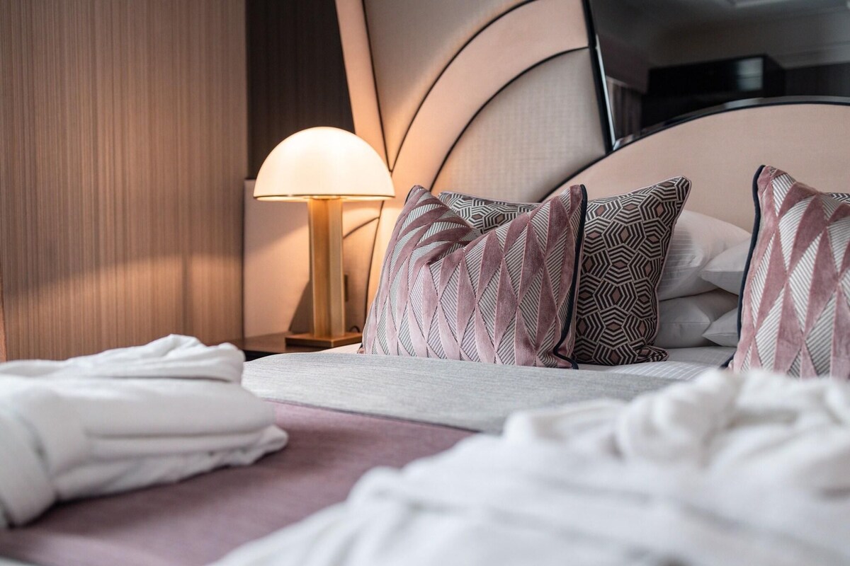 Uma cama bem arrumada com almofadas estampadas, um abajur e uma televisão em um móvel.