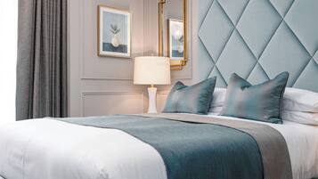 Un lit bien fait, recouvert d’une couverture blanche et turquoise, un miroir avec un cadre doré et une œuvre d’art encadrée accrochée au mur.