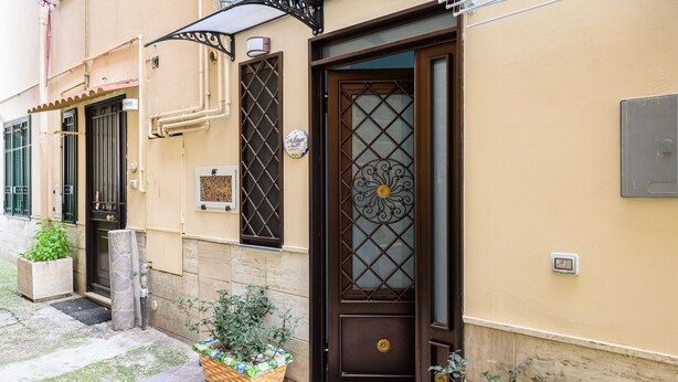A building with a brown door, a window with a metal grill, and a small garden area with a basket of plants. - Casa Maggio in Vietri sul Mare (Vietri sul Mare)
