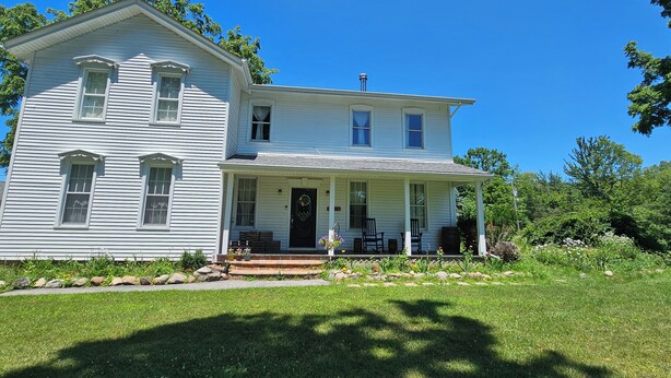 A two-story white house with a front porch, a chimney, and a small garden area. - Nature-Filled Family Retreat Near Ann Arbor I Gardens, Bonfire & Wildlife (Ann Arbor)