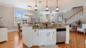 Una cocina amplia con una isla central, armarios blancos y lavavajillas. Hay luces colgantes sobre la isla y un ventilador de techo.
