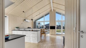 Een ruime keuken met een groot eiland, witte kasten en uitzicht op het buitenleven door grote ramen.