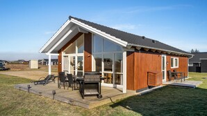 Een modern huis met een grote glazen deur, een houten terras en tuinmeubilair.