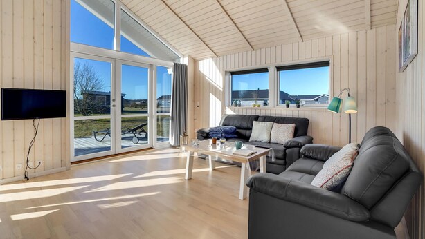 Een ruime woonkamer met een grote schuifpui naar een balkon, een flatscreen televisie aan de muur, een leren bank, een salontafel en een vloerlamp.