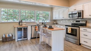 A modern kitchen with white cabinets, stainless steel appliances, and a large window with a view of greenery. - The Pelican Point (St. Augustine)