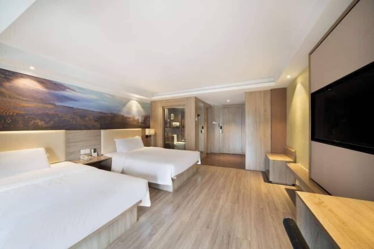 A hotel room with two beds, a TV, a painting on the wall, and a wooden floor.