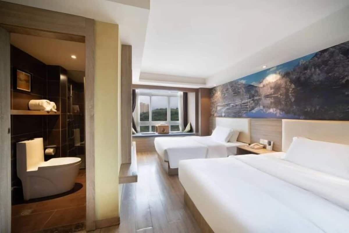 A hotel room with two beds, a bathroom, and a large window.