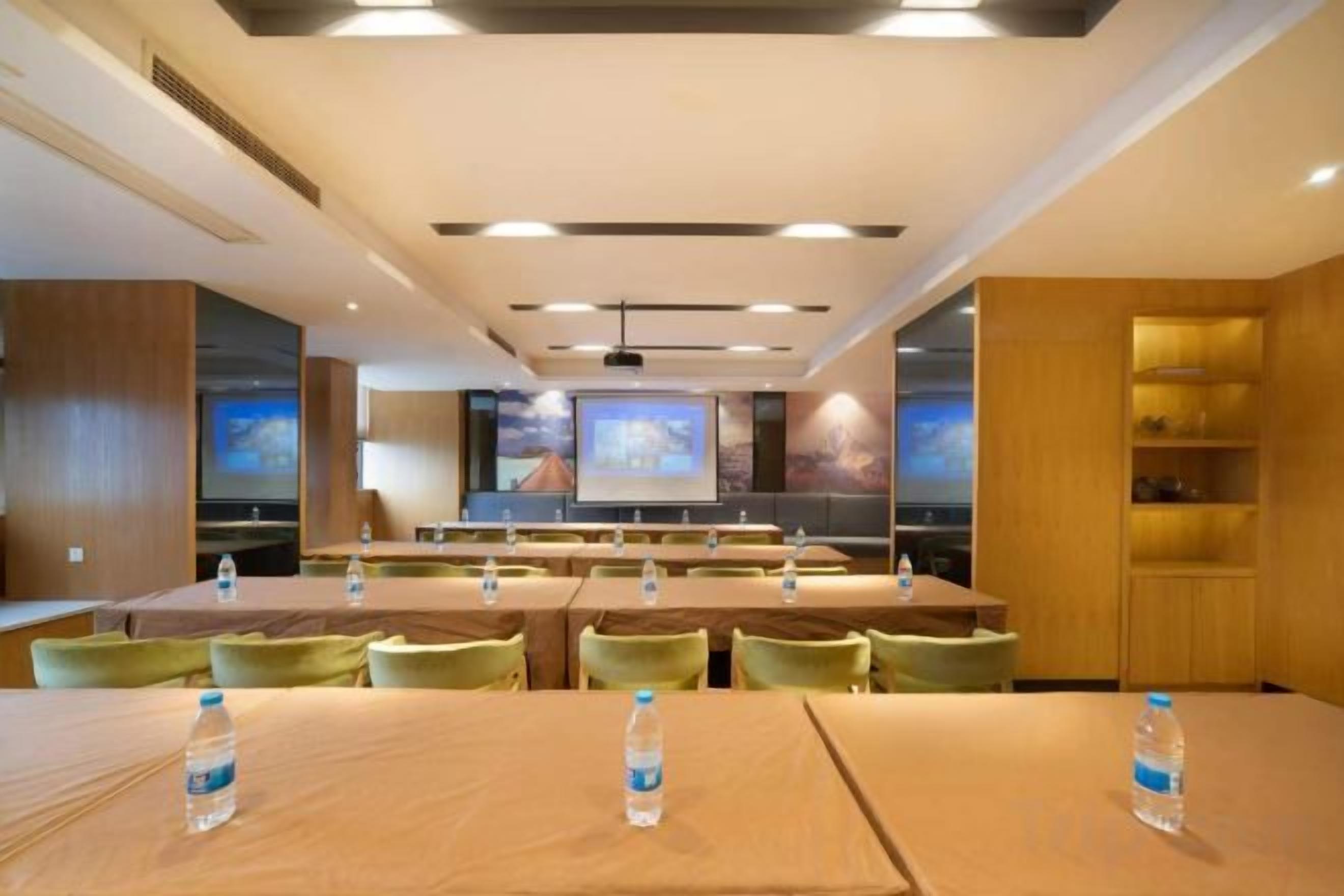 A conference room with multiple tables and chairs, equipped with water bottles, a projector screen, and a large screen displaying a landscape image.