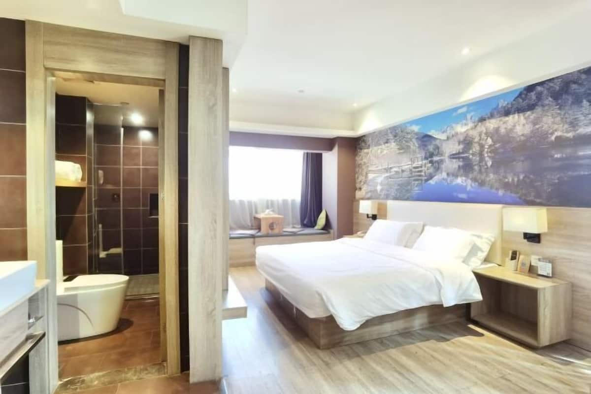 A hotel room with a bed, bedside tables, a bathroom with a shower, and a large window.