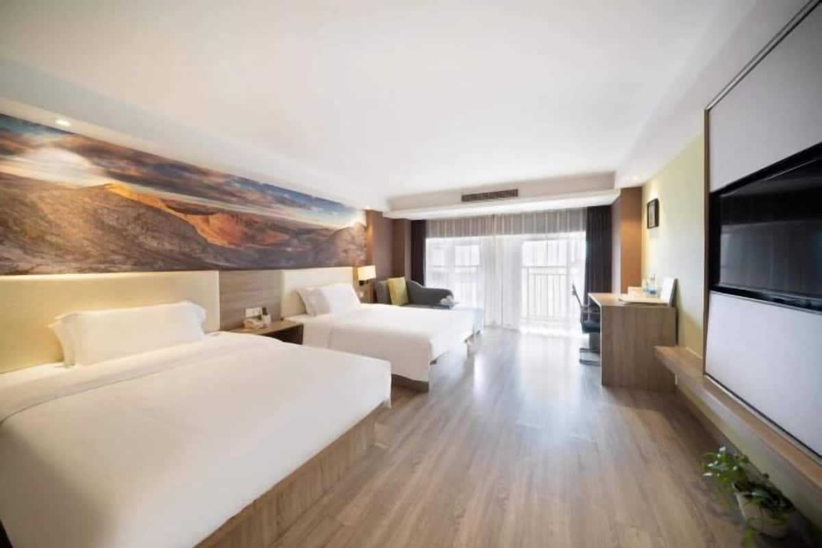 A hotel room with two beds, a large wall mural, a TV, and a desk with a chair.