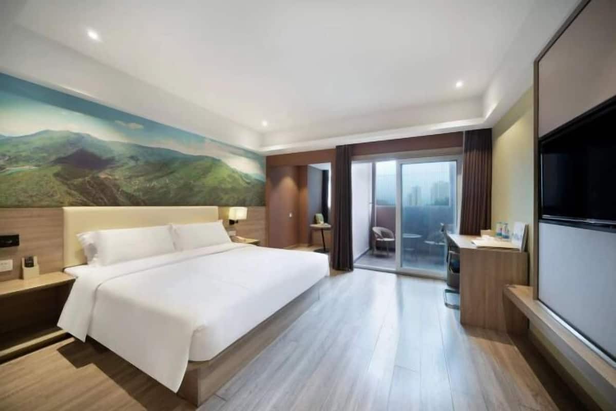 A hotel room with a large bed, a desk, a TV, and a painting of a landscape.