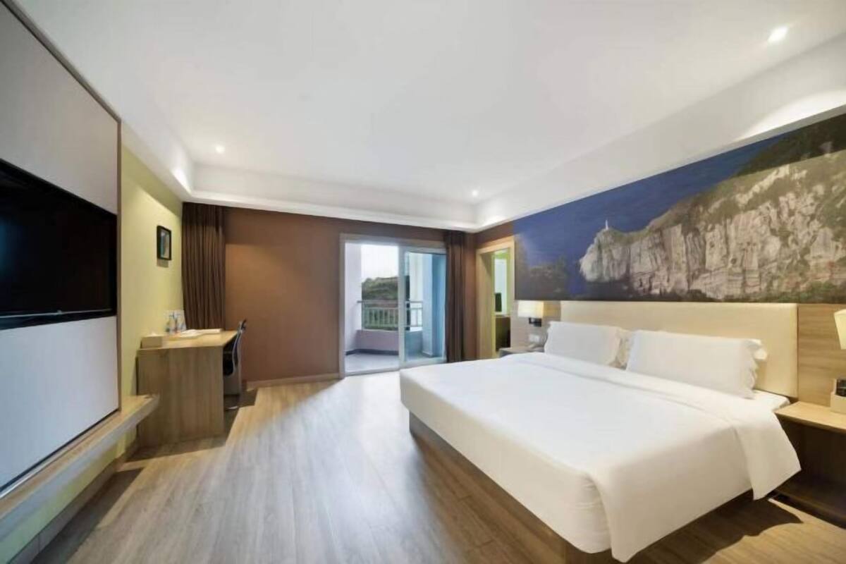 A hotel room with a large bed, a flat-screen TV, a desk, and a balcony.
