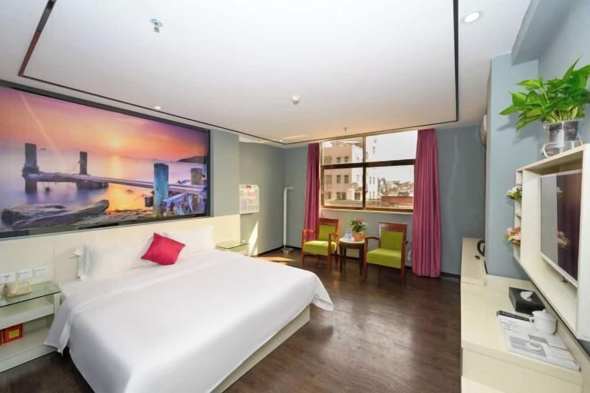 A hotel room with a large bed, a desk, a chair, a TV, and a window with curtains.